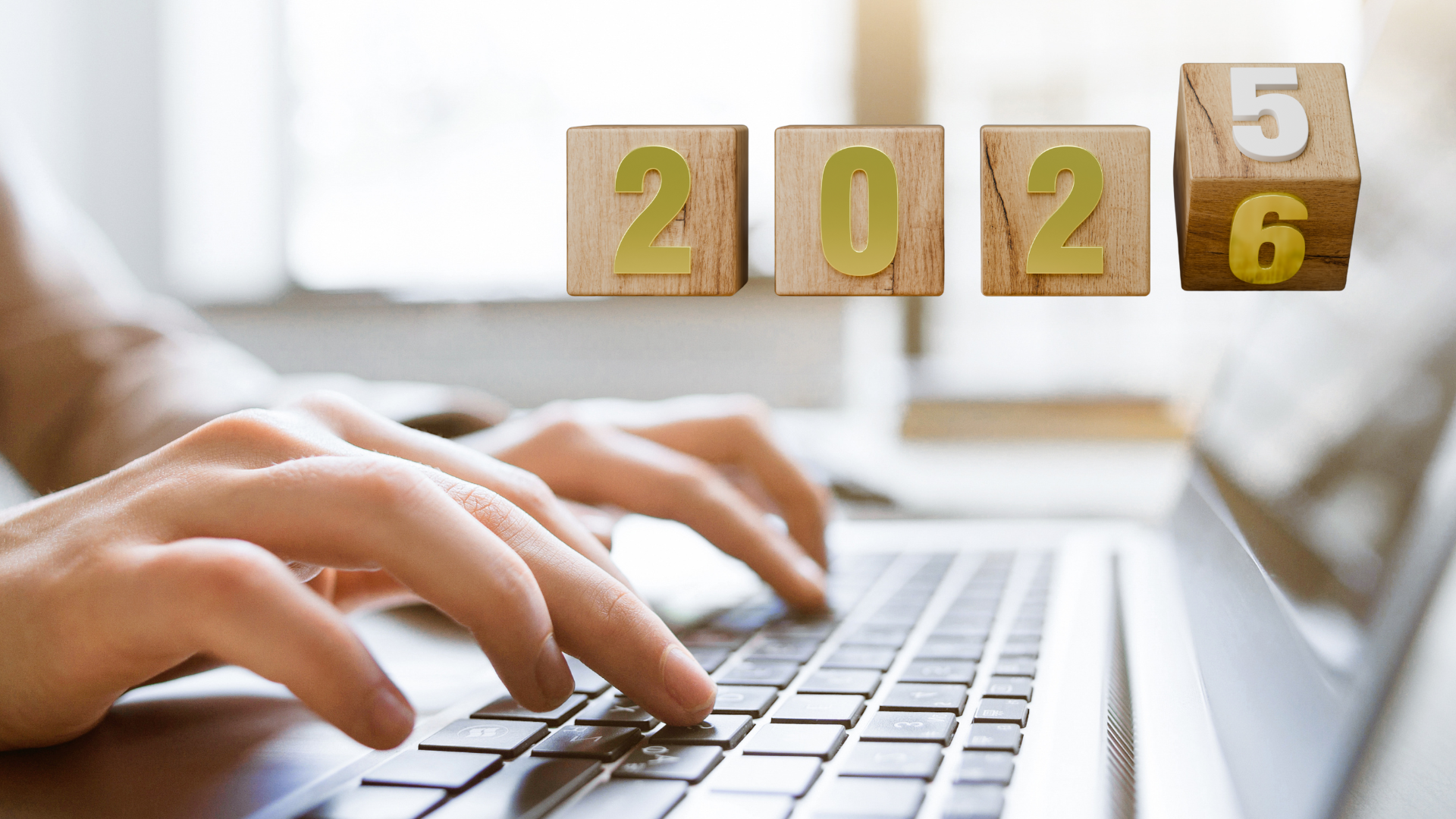 Close-up of hands typing on a laptop, with wooden blocks above showing the year 2025-2026